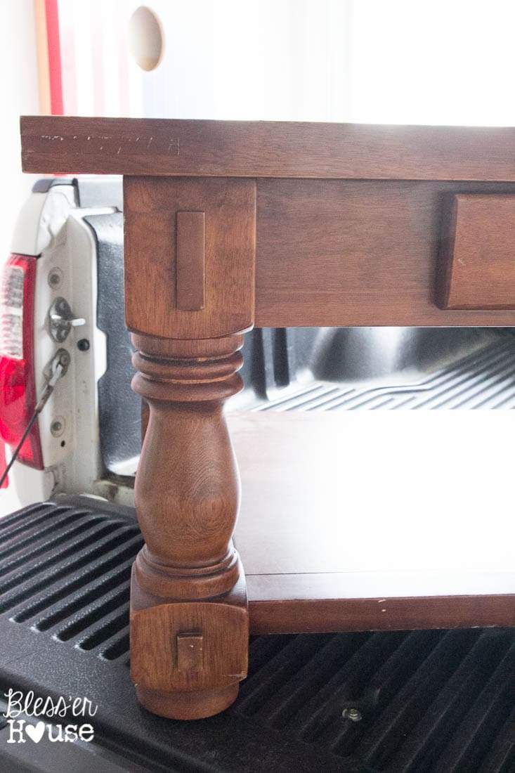Close-up of the elegant, turned legs of a thrift store coffee table, highlighting its beautiful shape before undergoing a farmhouse-style chippy white makeover.