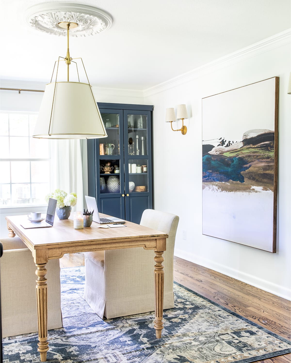 home office for two with work table and rolling arm chairs, white walls, navy blue storage cabinets, oversized art, and black French doors