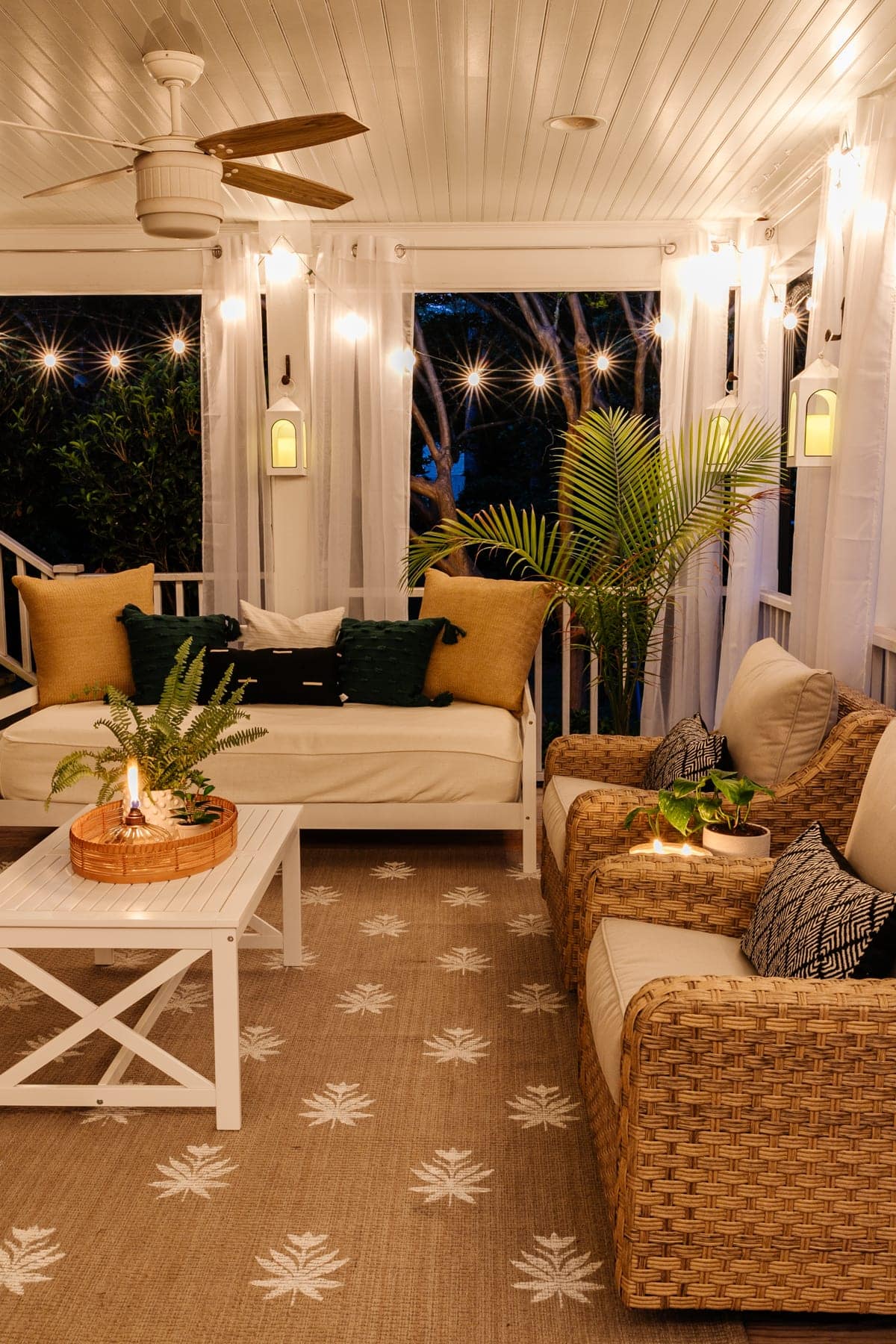 back porch after with mosquito net curtains, string lights, outdoor day bed, outdoor conversation set, and floral block outdoor rug