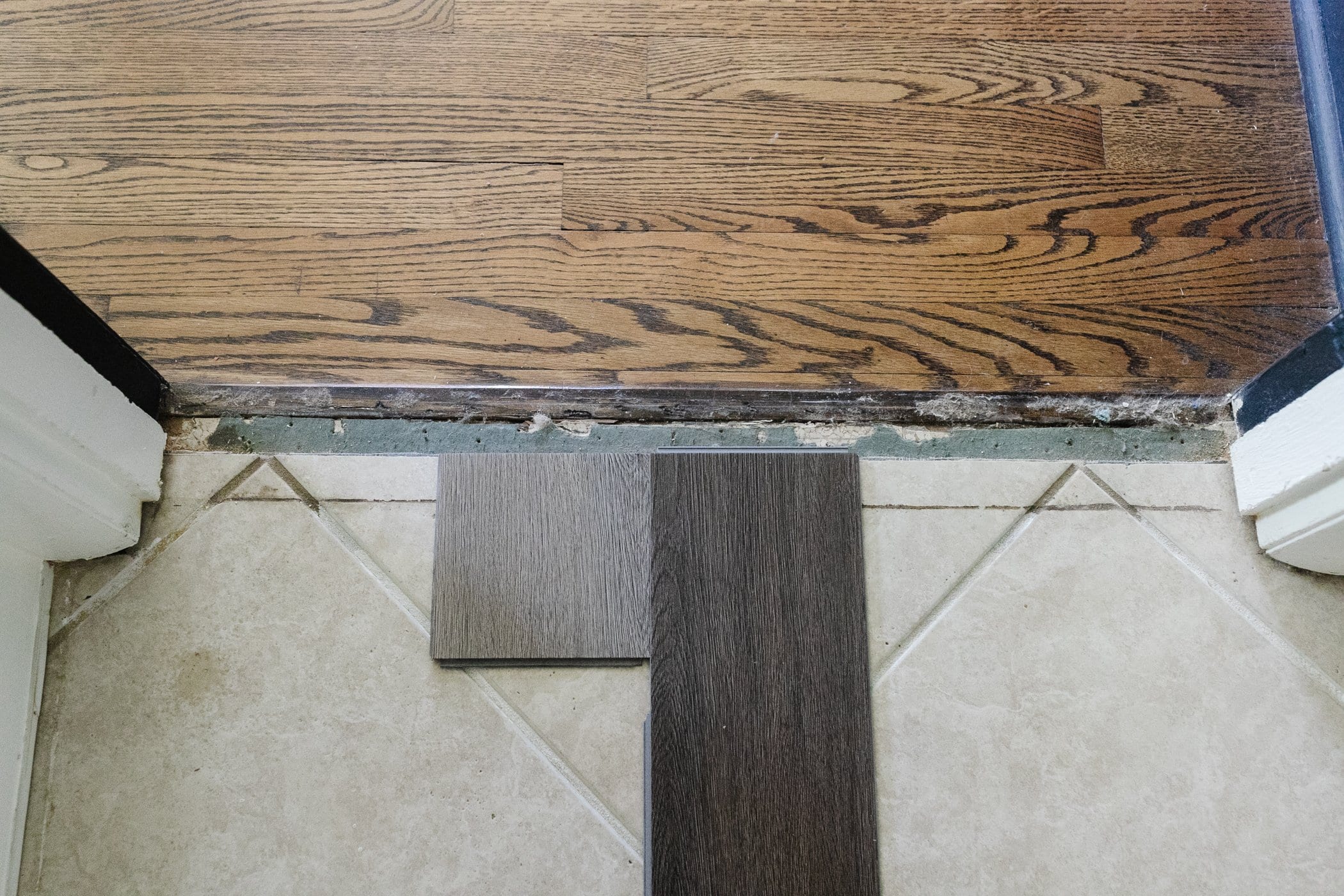 Light beige and dark brown herringbone LVP floor samples on top of beige tile