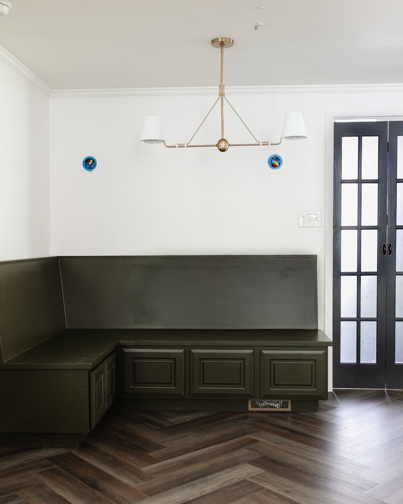 corner banquette in a breakfast nook with linear chandelier, herringbone floor, and French door