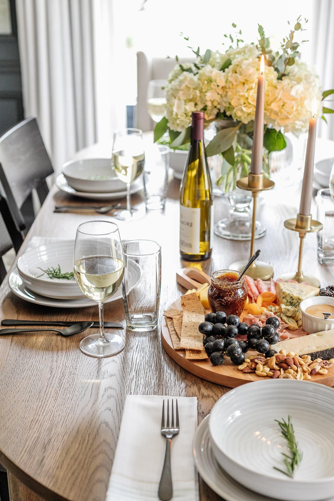 dinner table decor with simple place setting, wine glasses, charcuterie board, candlesticks, and vase of flowers