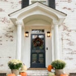 front porch decorated for fall with fake pumpkins and mums on porch steps with limewashed brick