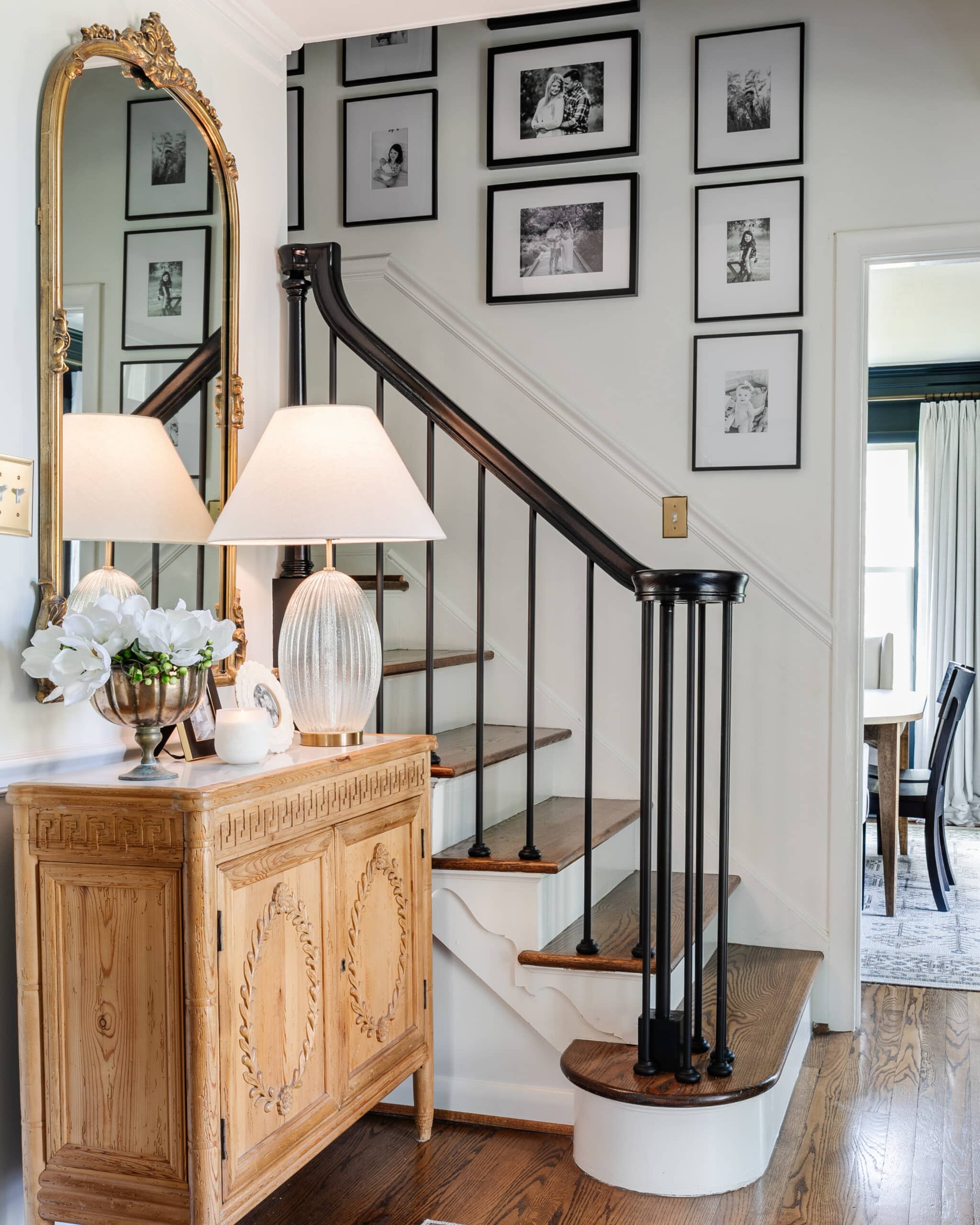 gallery wall on stairs in an entryway with accent chest, mirror, and lamp