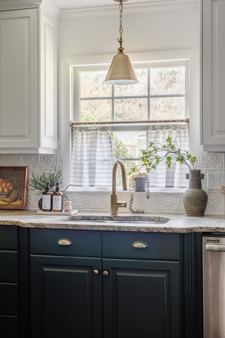 kitchen sink window with striped cafe curtains, white upper cabinets, green lower cabinets, and pressed tin backsplash