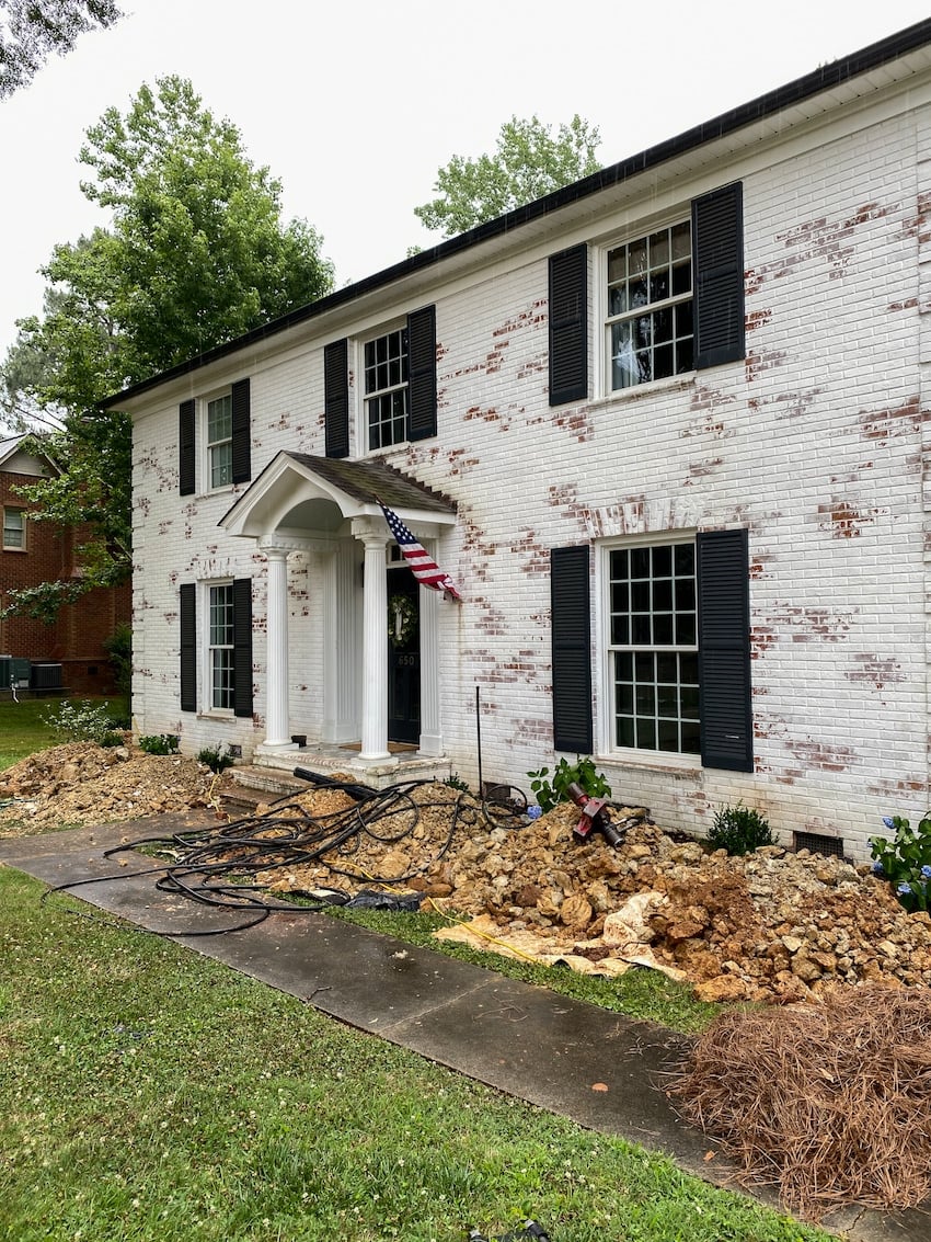 foundation repairs in front of a brick house with dug up flower beds